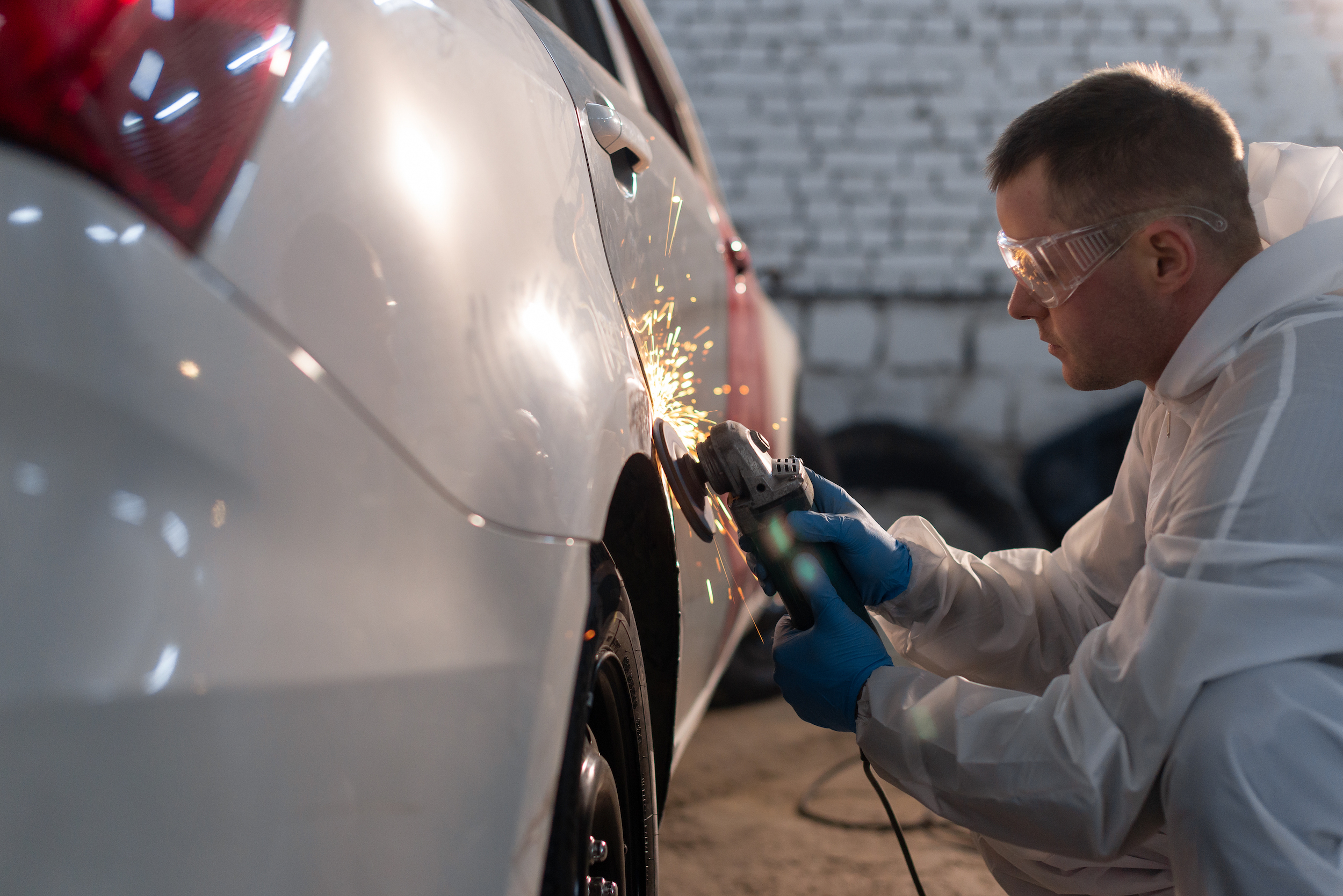 Car repair at a service station. The master fixes a broken door with a grinder